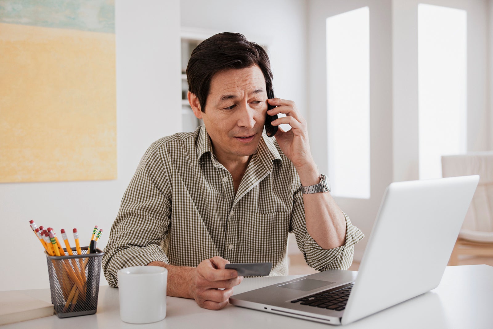 A man holding a credit card while on the phone in front of a laptop