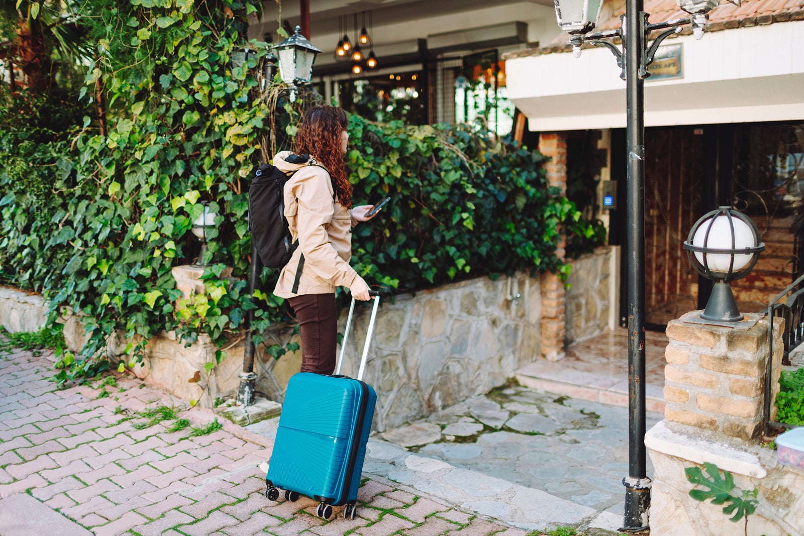 woman with suitcase entering ivy-covered building