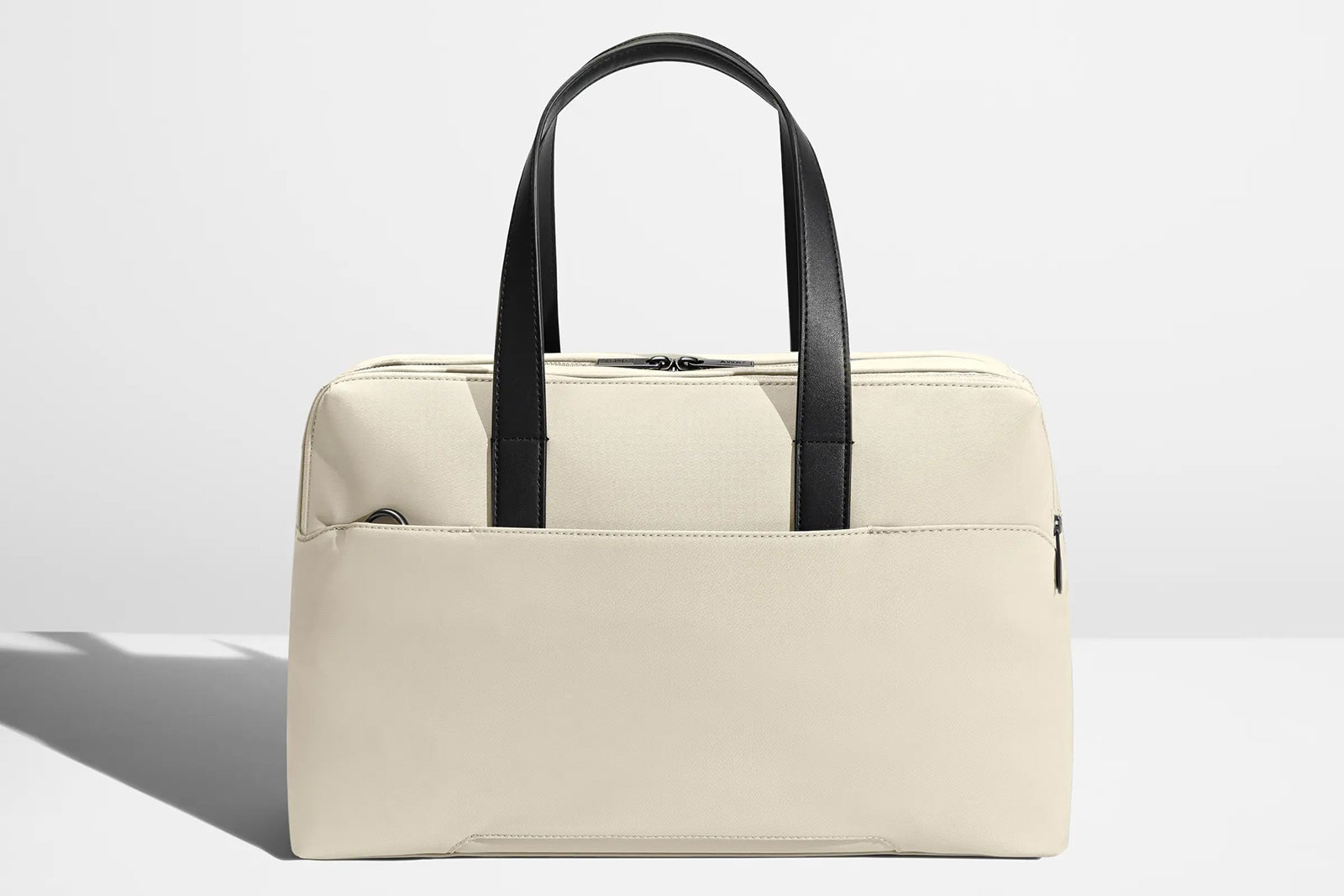 a cream-colored handbag with black handles