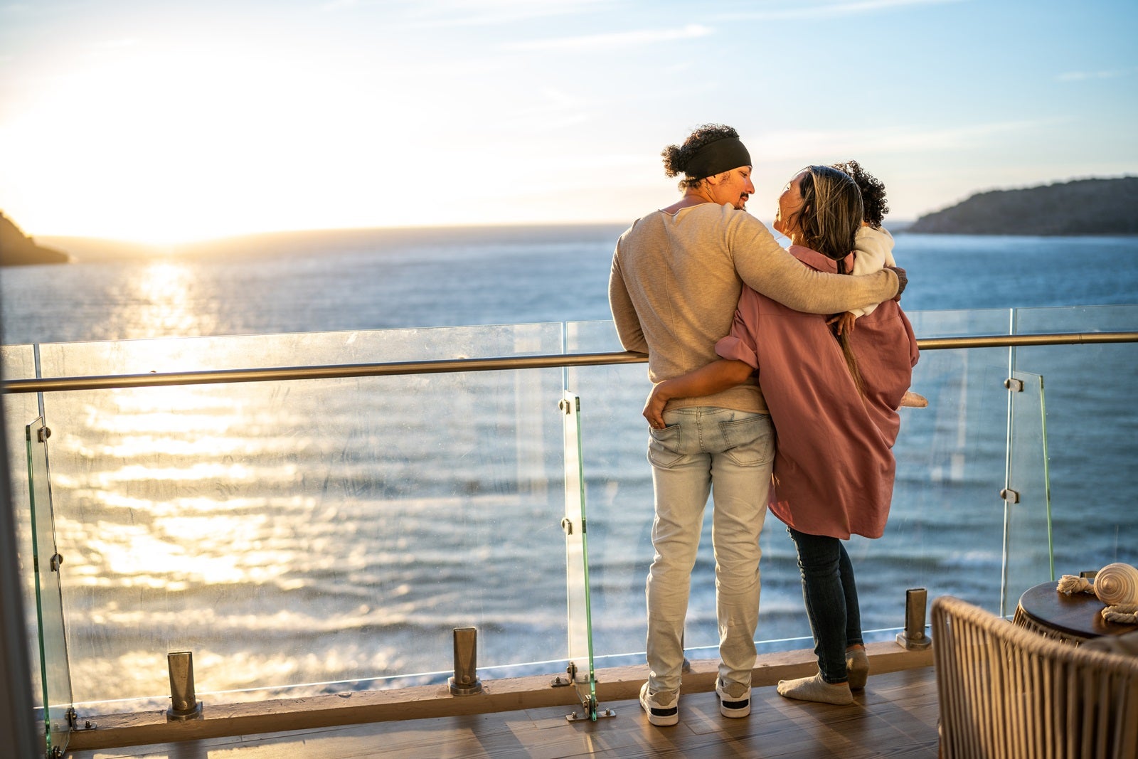 A young family stand on the deck of a cruise ship at sunset