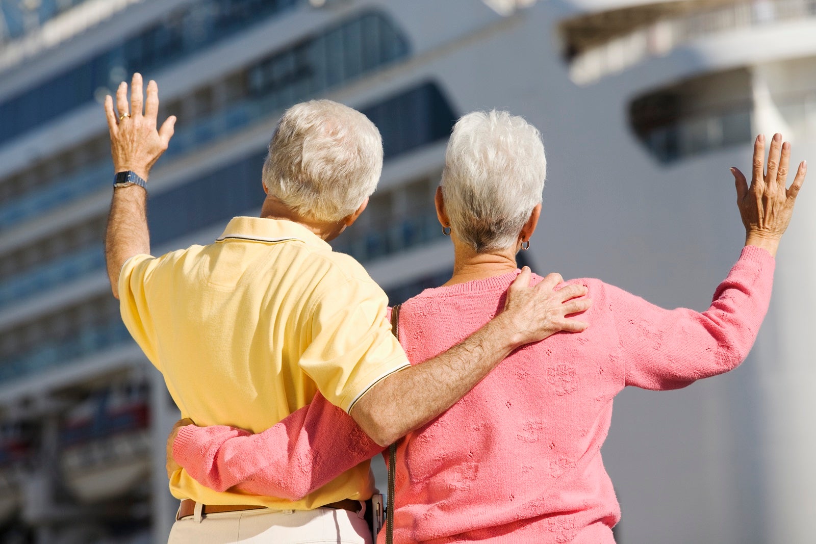 A couple with their back to the camera waving at a departing cruise ship