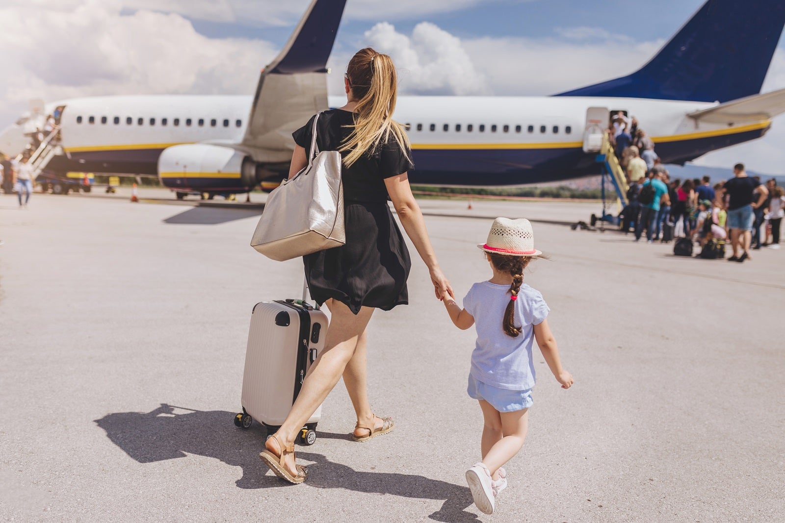 Woman with luggage holding daughter's hand and walking toward a plane to board it