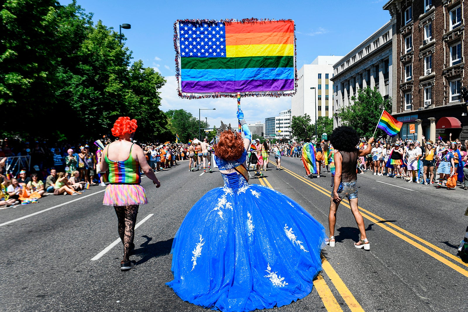 person in blue ballgown raising rainbow flag in Denver pride parade