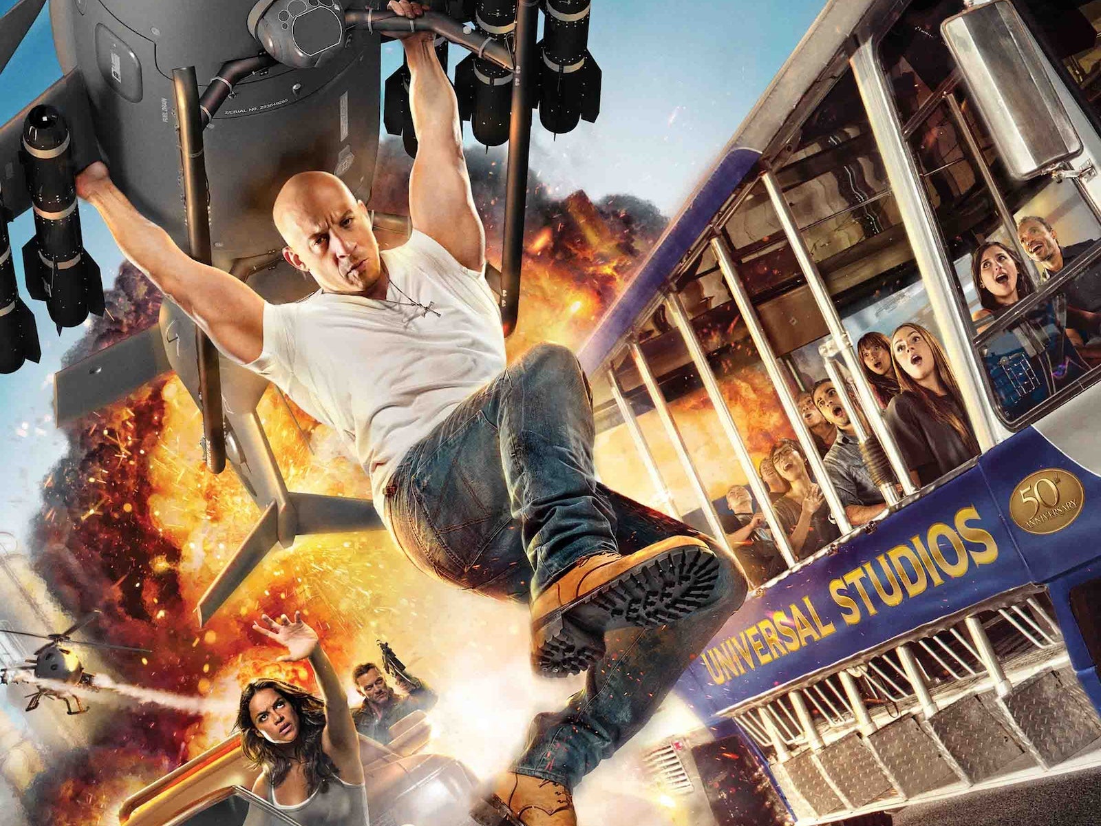 Vin Diesel hanging onto a helicopter as an explosion occurs behind him and people look on in a Universal Studios tour bus