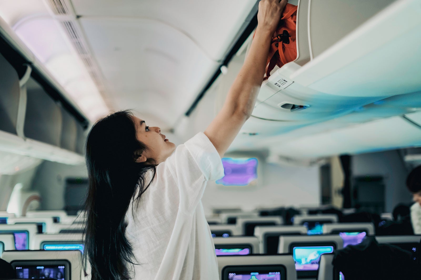 A woman putting away her bag in the overhead compartment