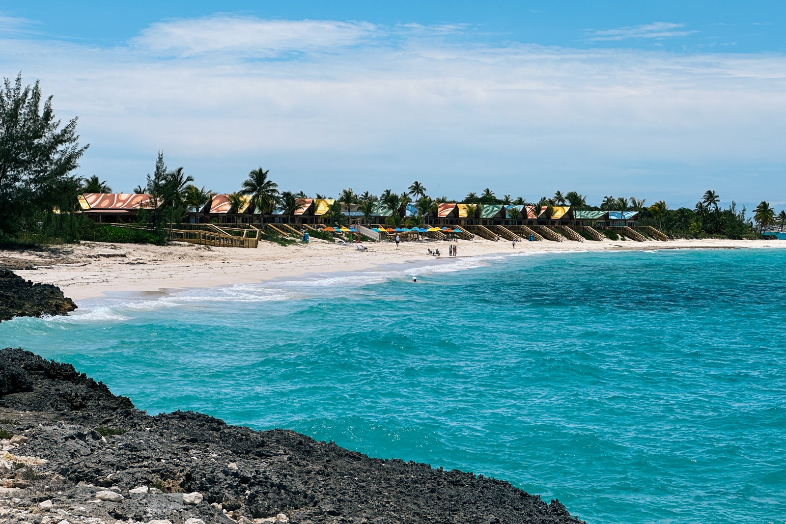 A view of sandy shoreline with cabanas and colorful umbrellas, taken from nearby rocks