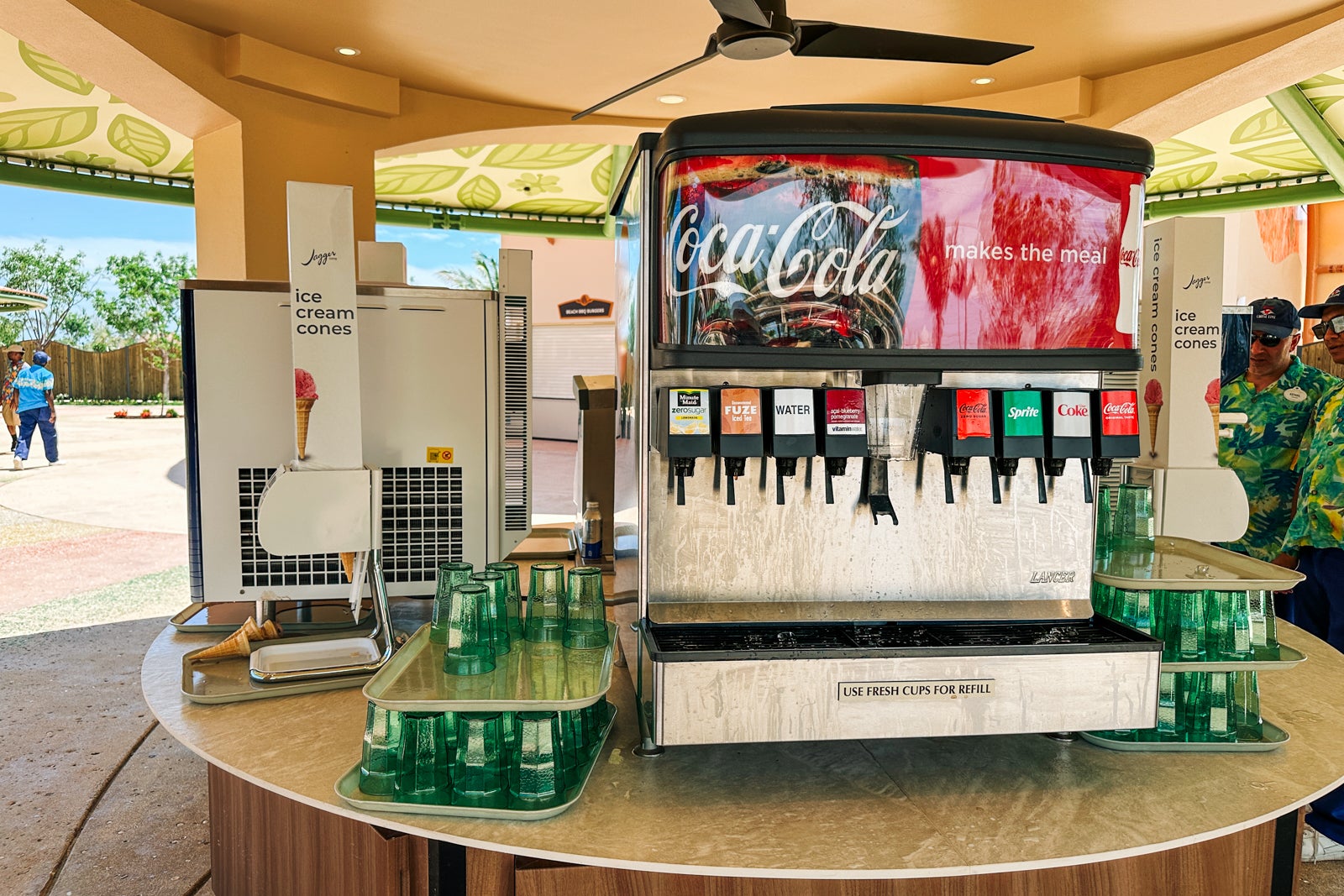 A soda dispenser with cups beside it