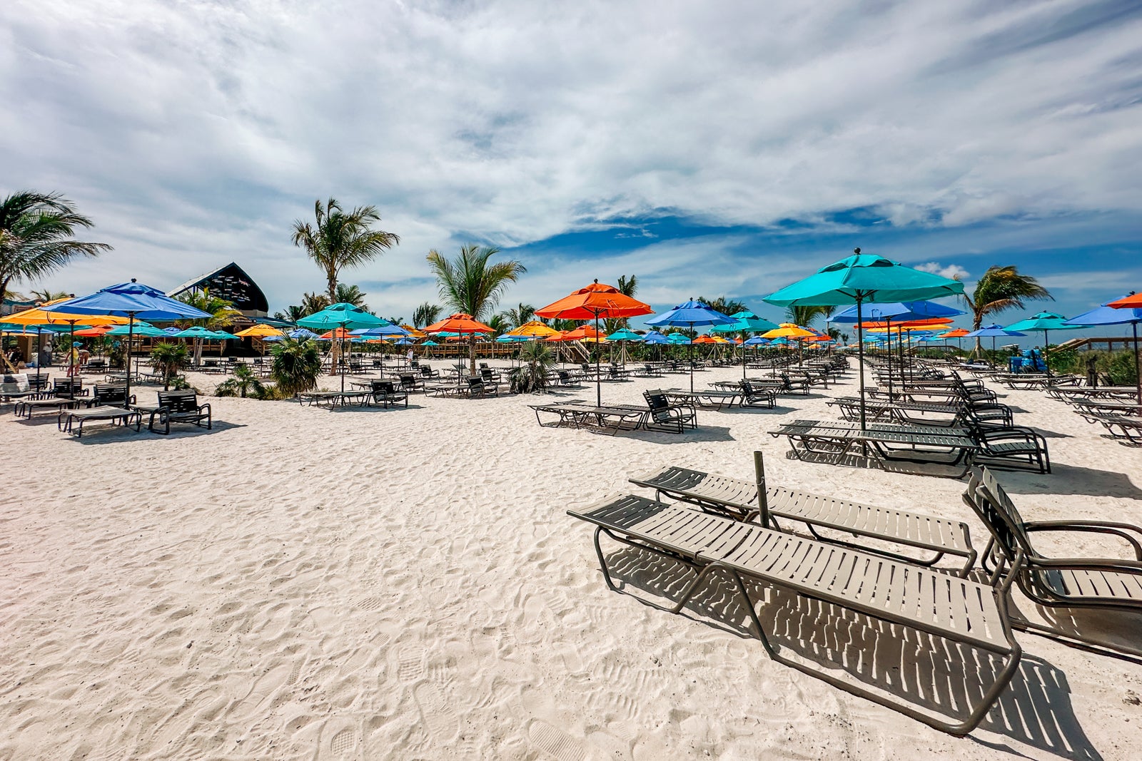 A beach with lounge chairs, colorful umbrellas and palm trees