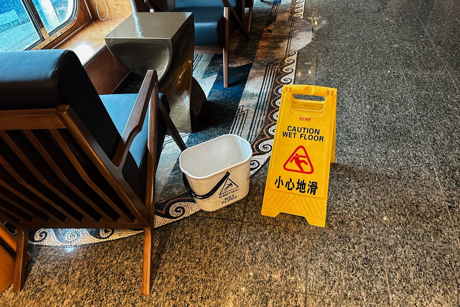 A bucket catching leaking water between a blue chair and a caution sign