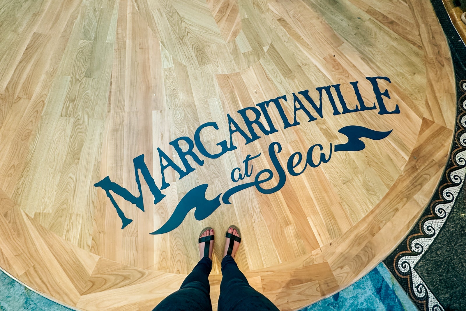 A pair of sandaled feet standing on a wooden floor with the words "Margaritaville at Sea" printed on it