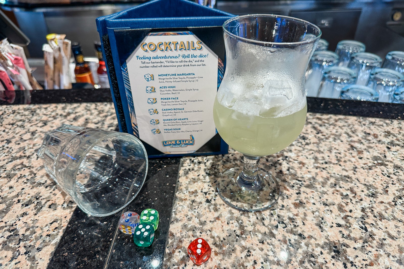 A bar menu with a drink next to it and a glass on its side with dice spillig out