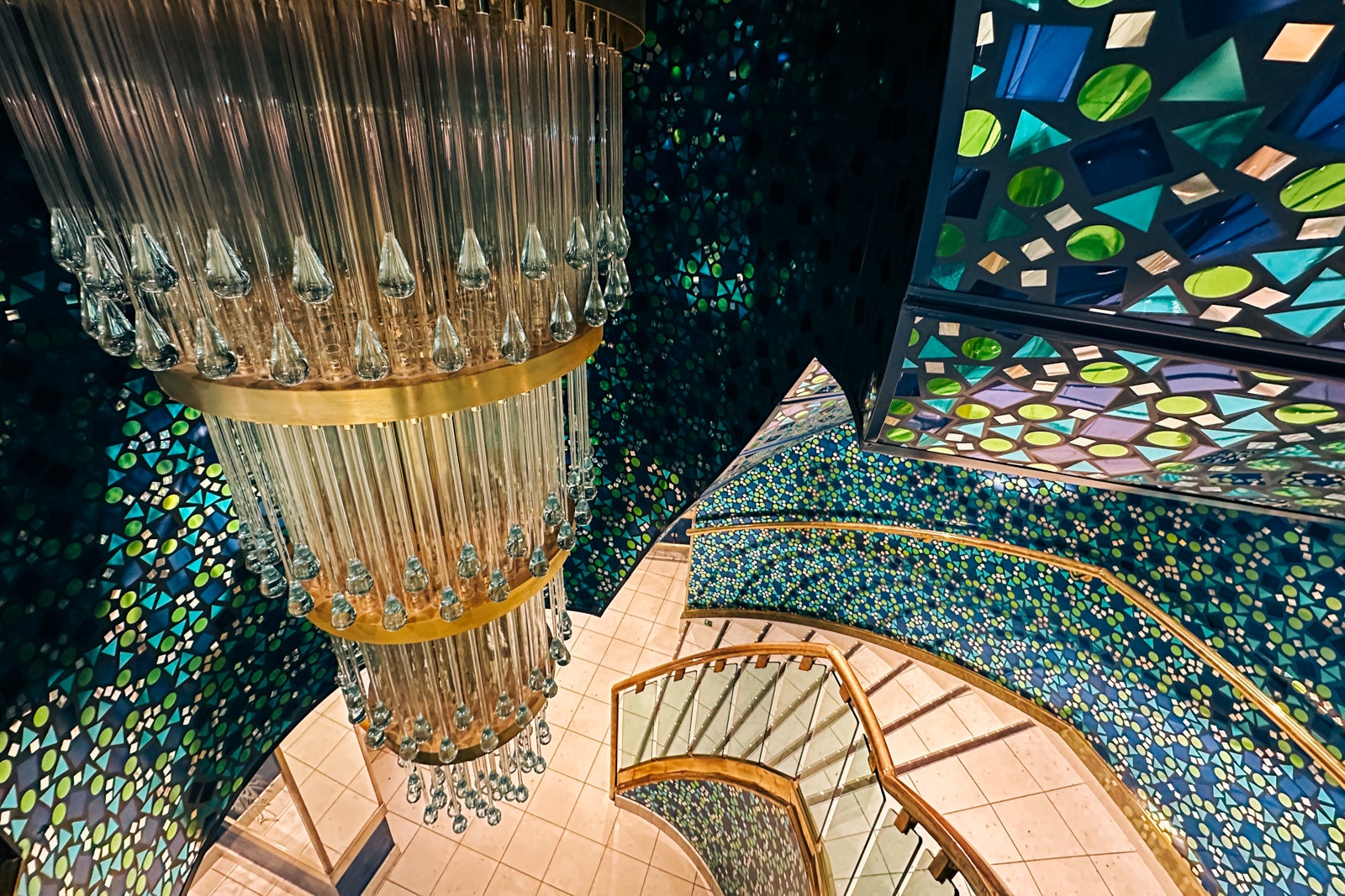 A Joe Farcus-designed staircase with a chandelier and walls with blue and green mosaic mirror pieces