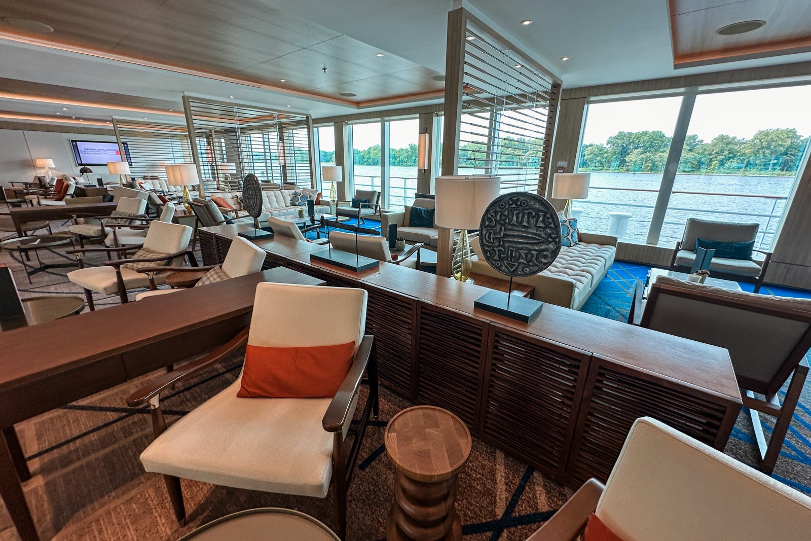 A neutral-colored lounge area with light woods, seating with white cushions and blue and orange accent pillows