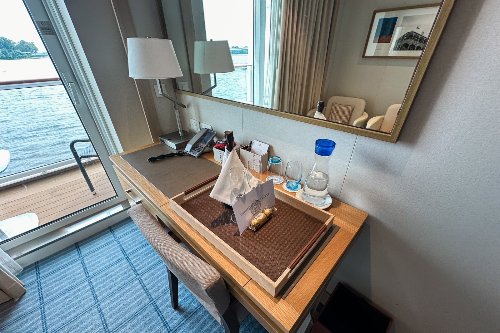 A cruise cabin desk/vanity area with a lamp, water carafe, phone and room service tray