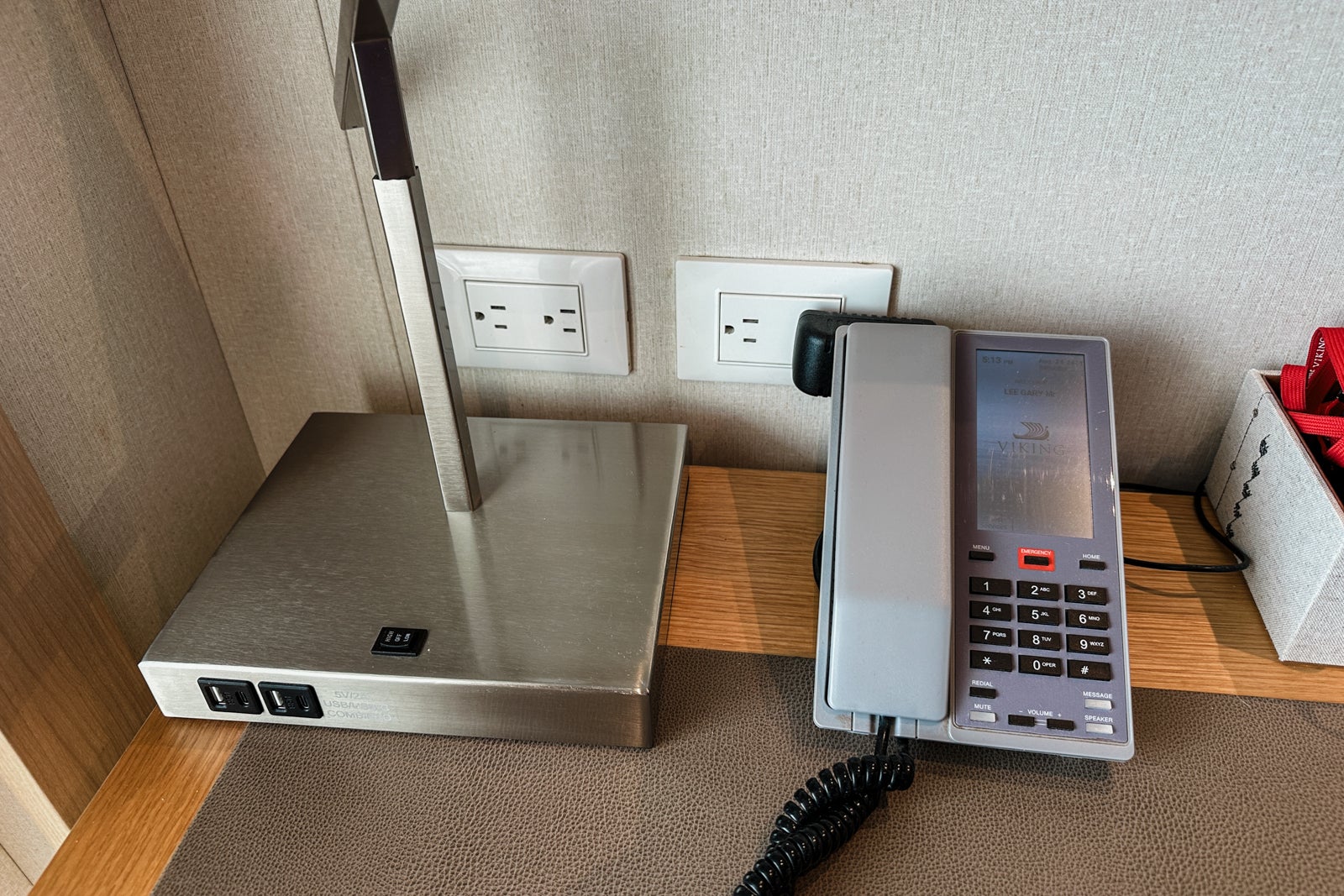 Outlets near a cruise ship cabin vanity with a lamp and a phone in front of them