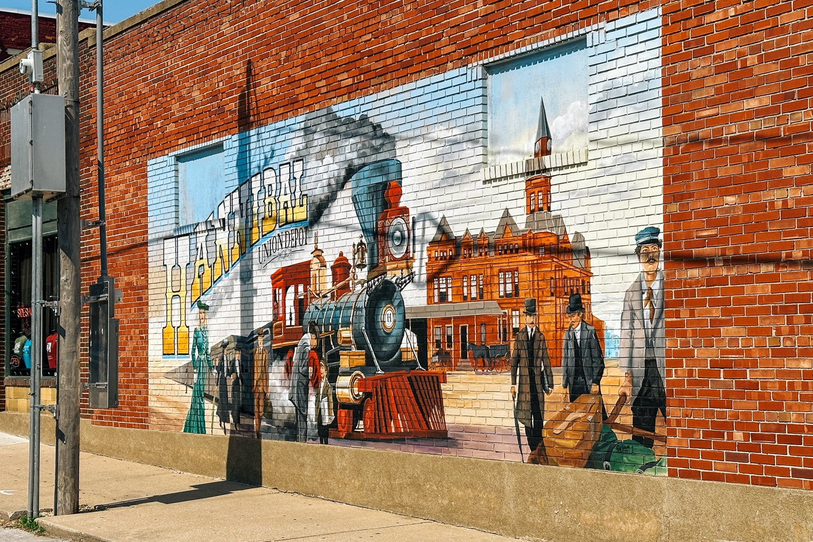 A likeness of a postcard painted on the side of a brick building, reading "Hannibal" with a train 