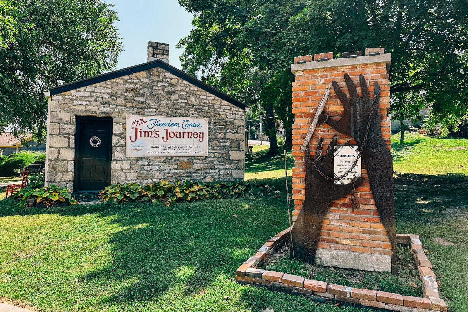 A stone building with a sign reading "Jim's Journey: Freedom Center African American Life History Project" and a brick wall with a sculpture of an enslaved person's hands