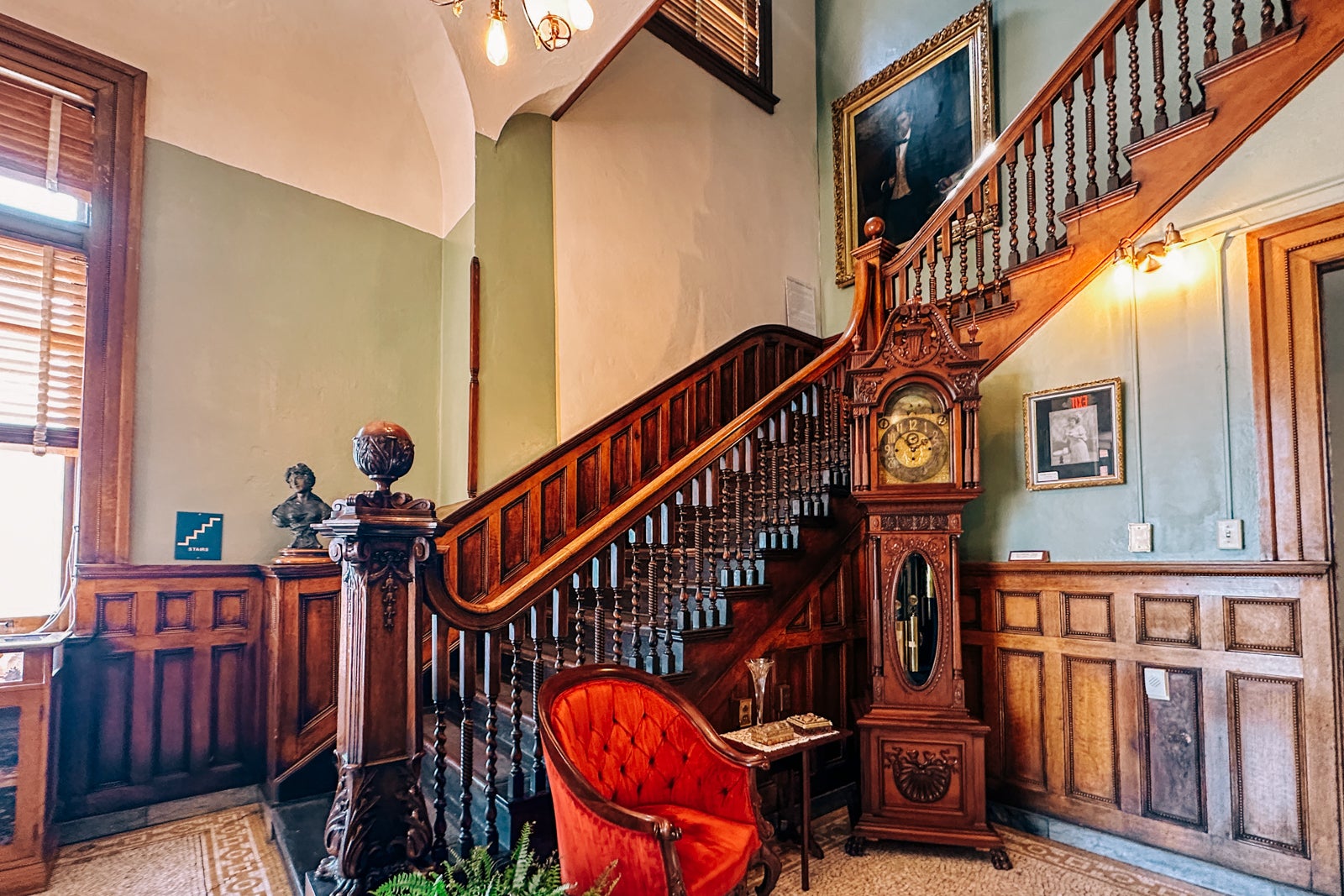 A grand staircase with a tufted chair and grandfather clock