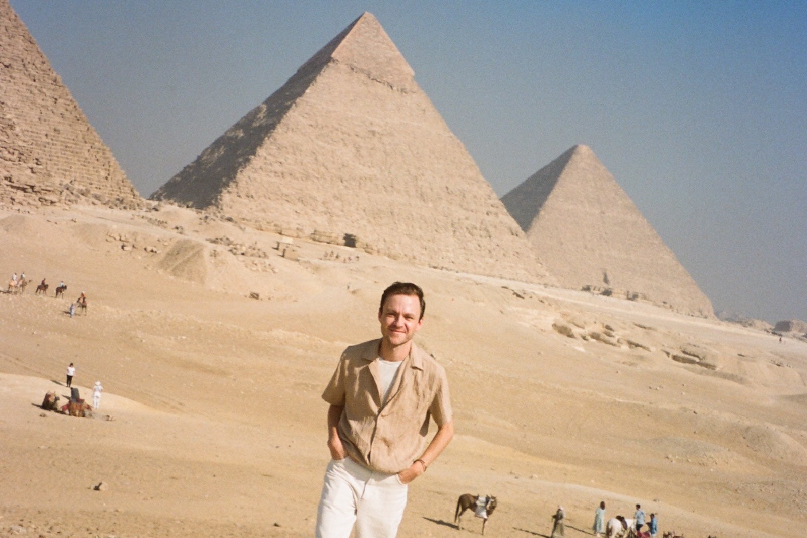 Man in beige and white standing in front of the pyramids in Egypt