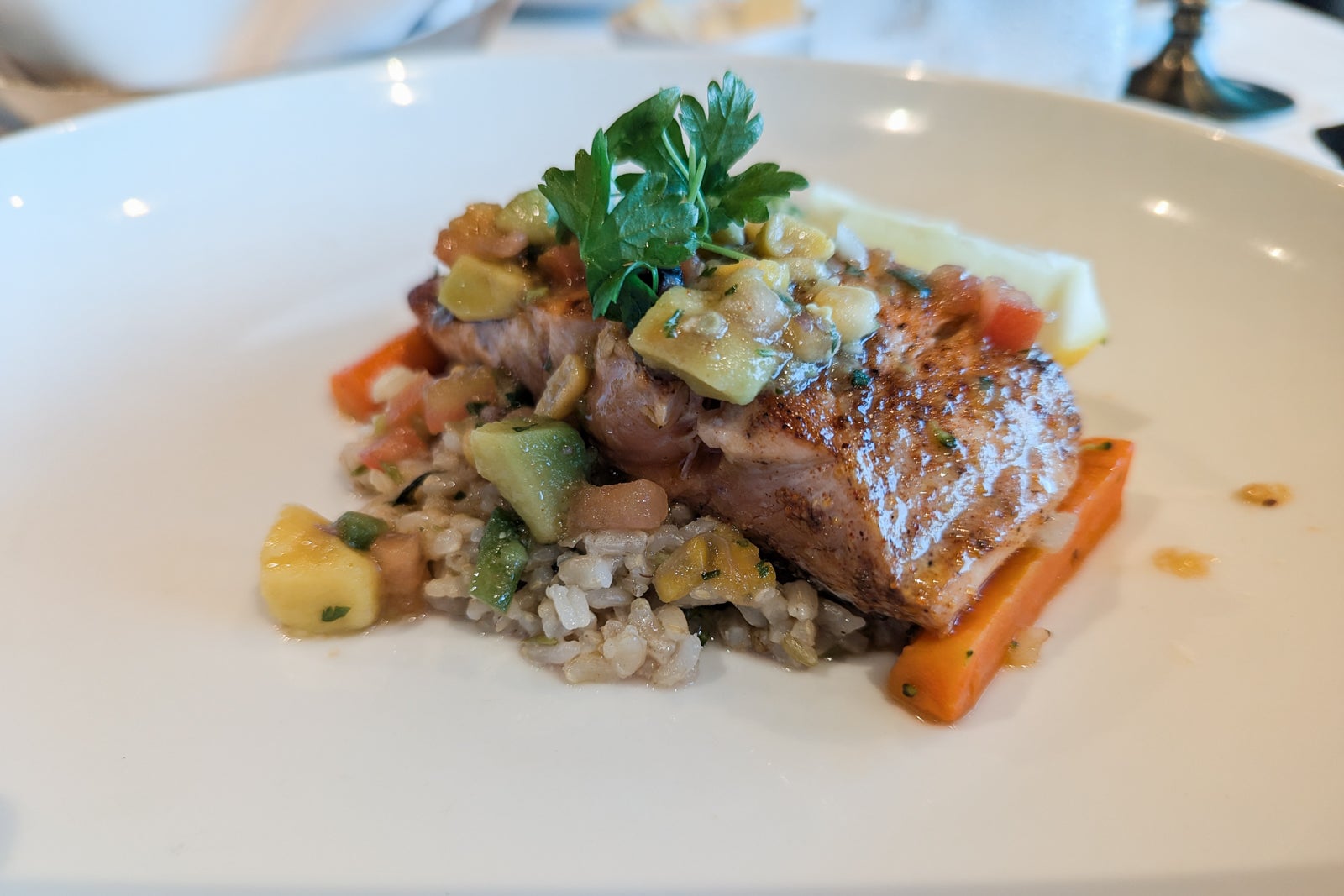 Salmon topped with avocado and mango on a white plate