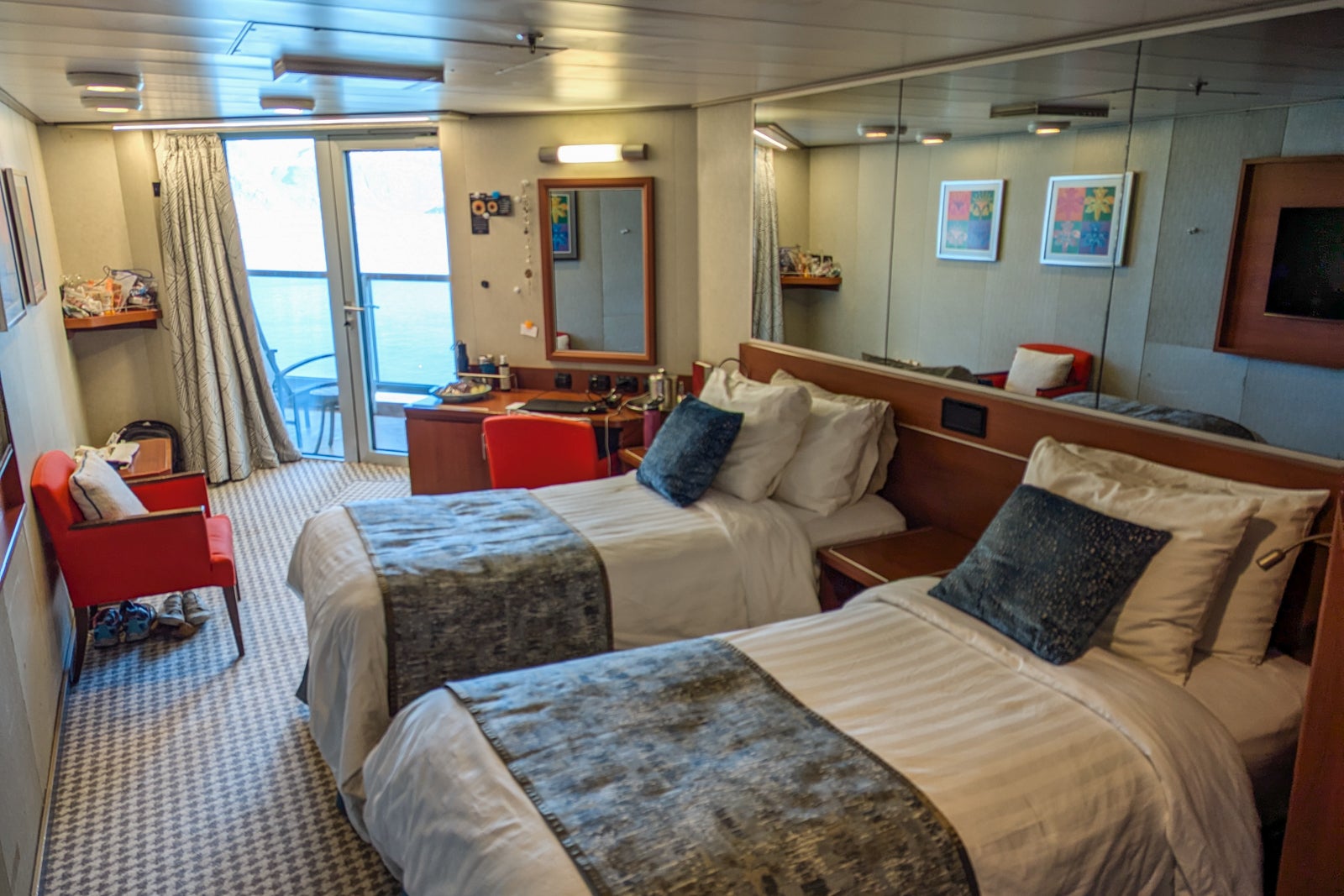 Cruise ship cabin with two twin beds, red chairs and wood desk