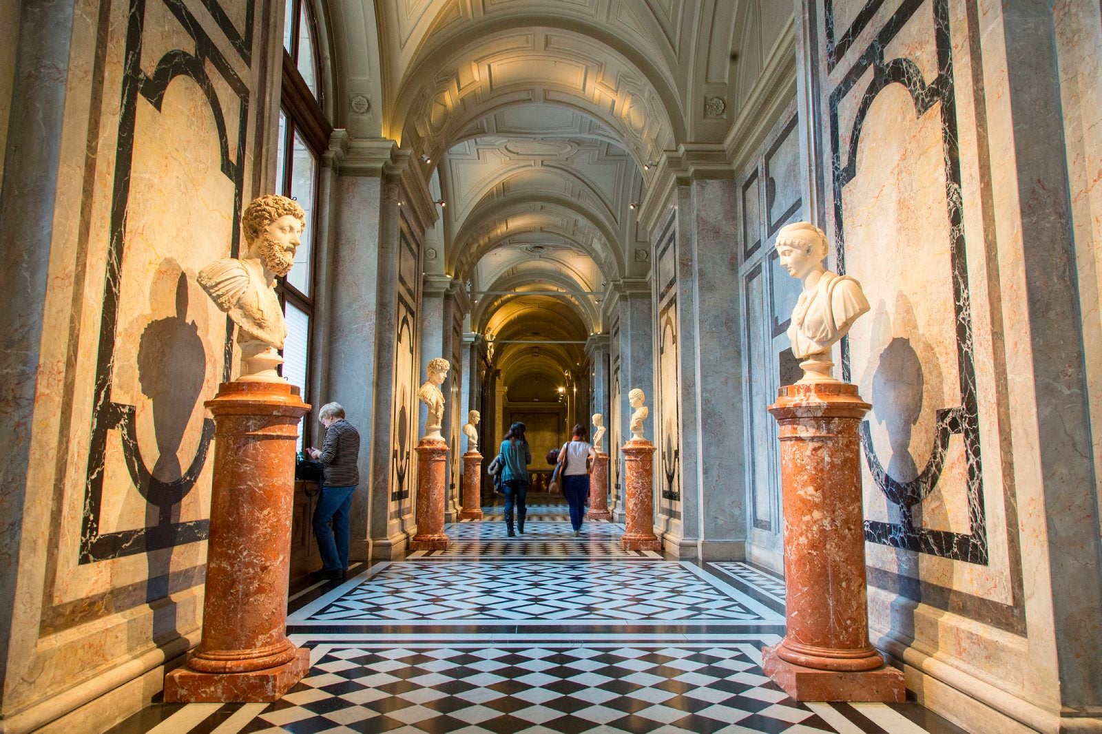 People walking through museum hall with marble busts