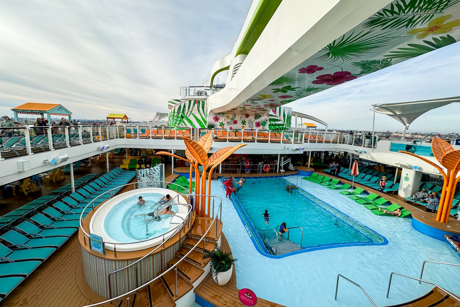 A cruise ship pool deck with sun loungers and a hot tub