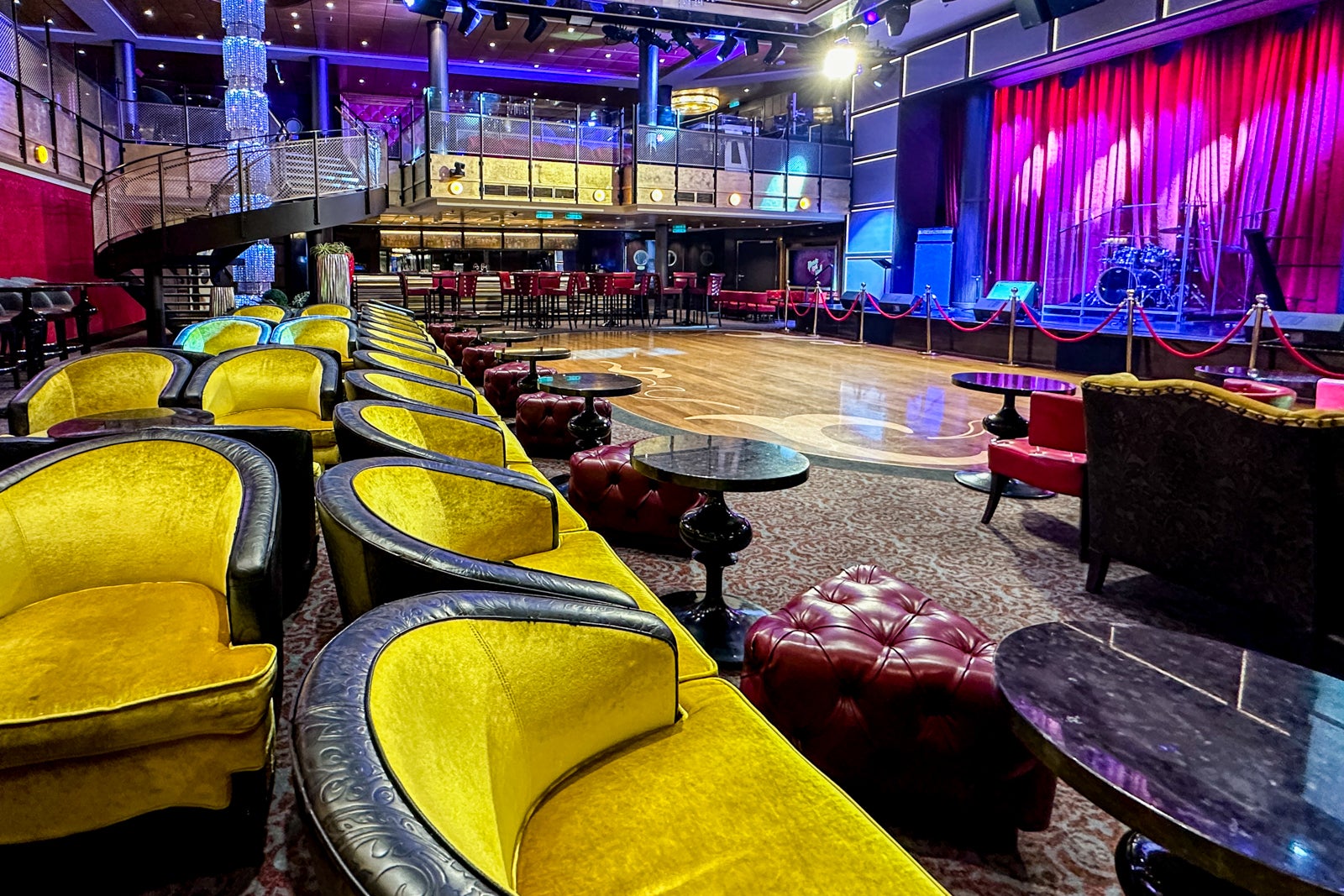 A colorful two-deck lounge on a cruise ship with a stage, a dance floor and bright yellow upholsetered chairs