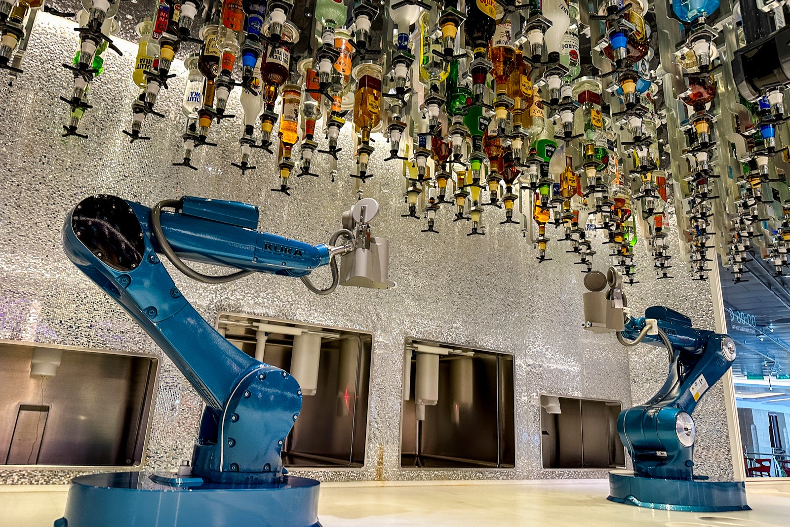 A bar staffed by robotic arms with bottles of alcohol hanging overhead