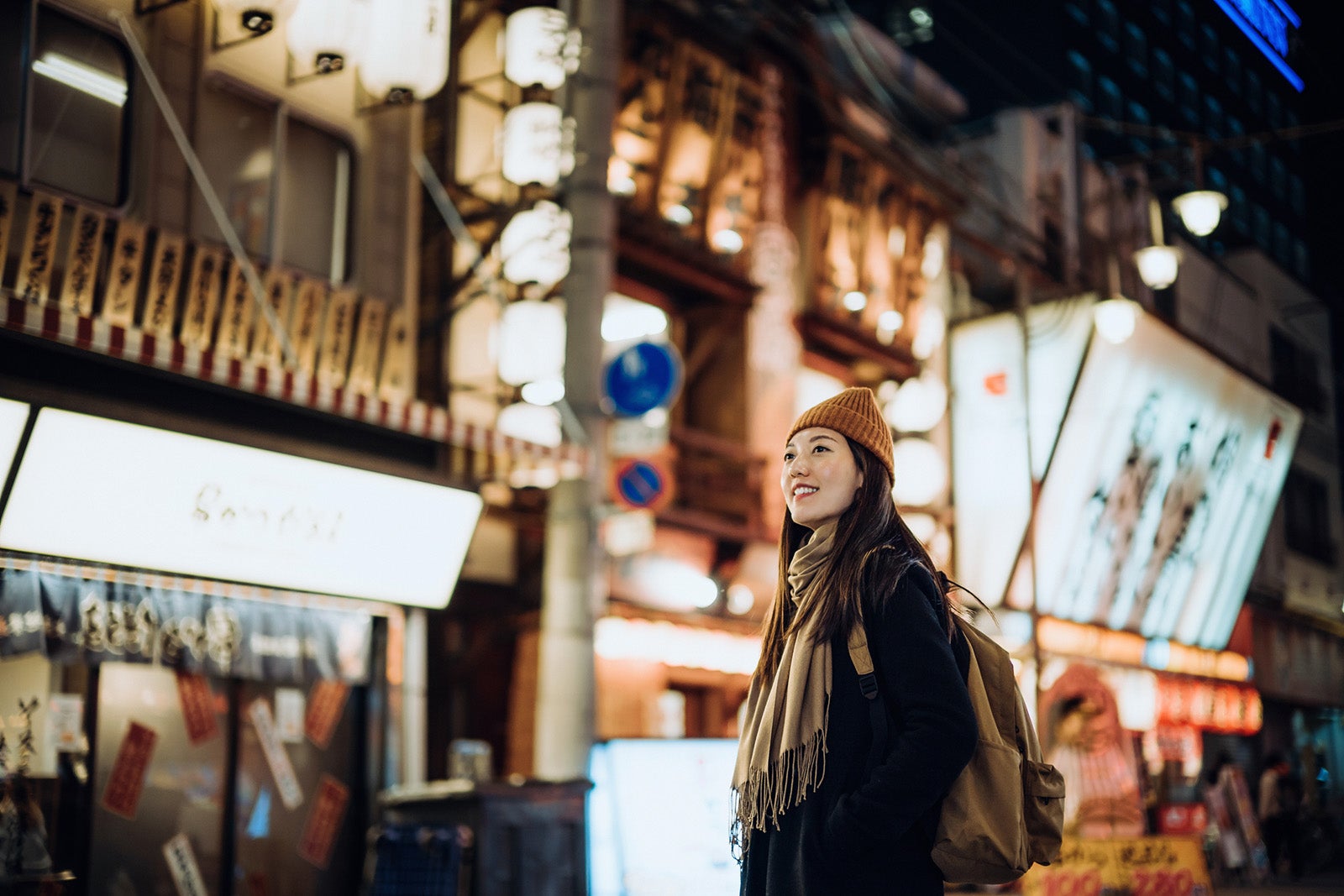 Young Asian female traveller with backpack visiting Japan, exploring and strolling in downtown city street at night in Osaka. A popular nightlife and entertainment area in the city. Travel, vacation and holiday concept