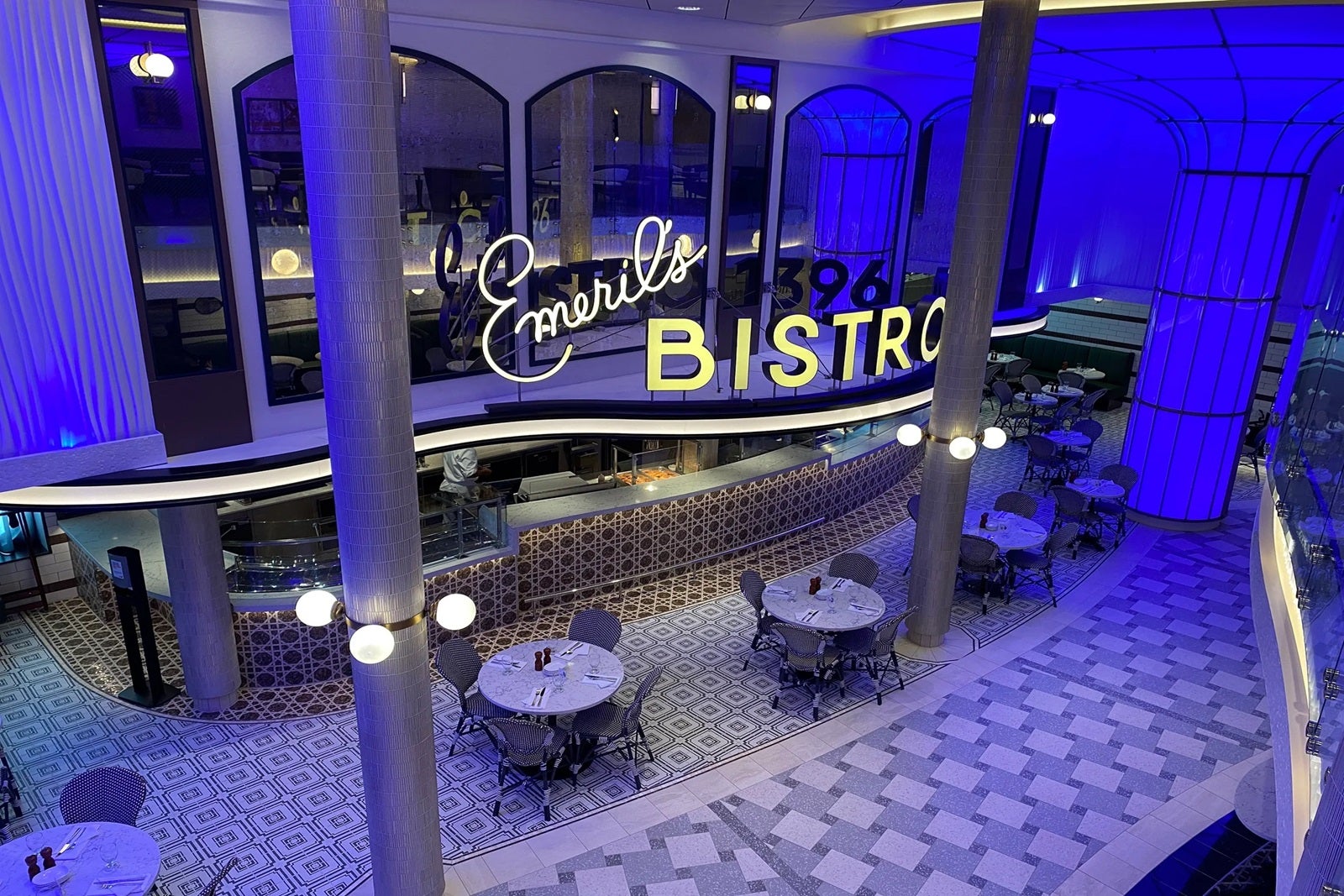 A view of a cruise ship restaurant from above with purple lighting, tables, pillars and a sign that says 