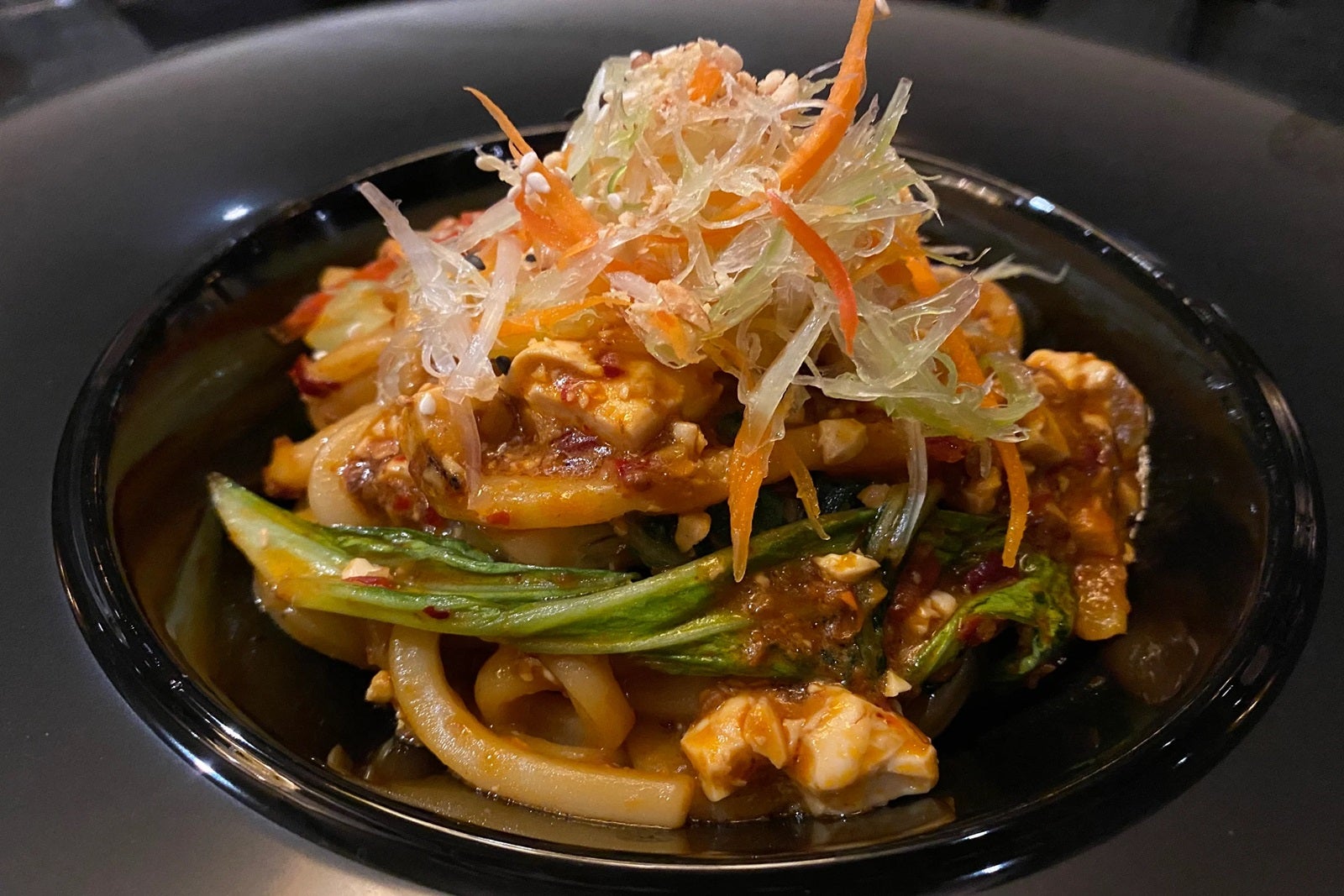 A black plate of Chinese dandan noodles topped with vegetables