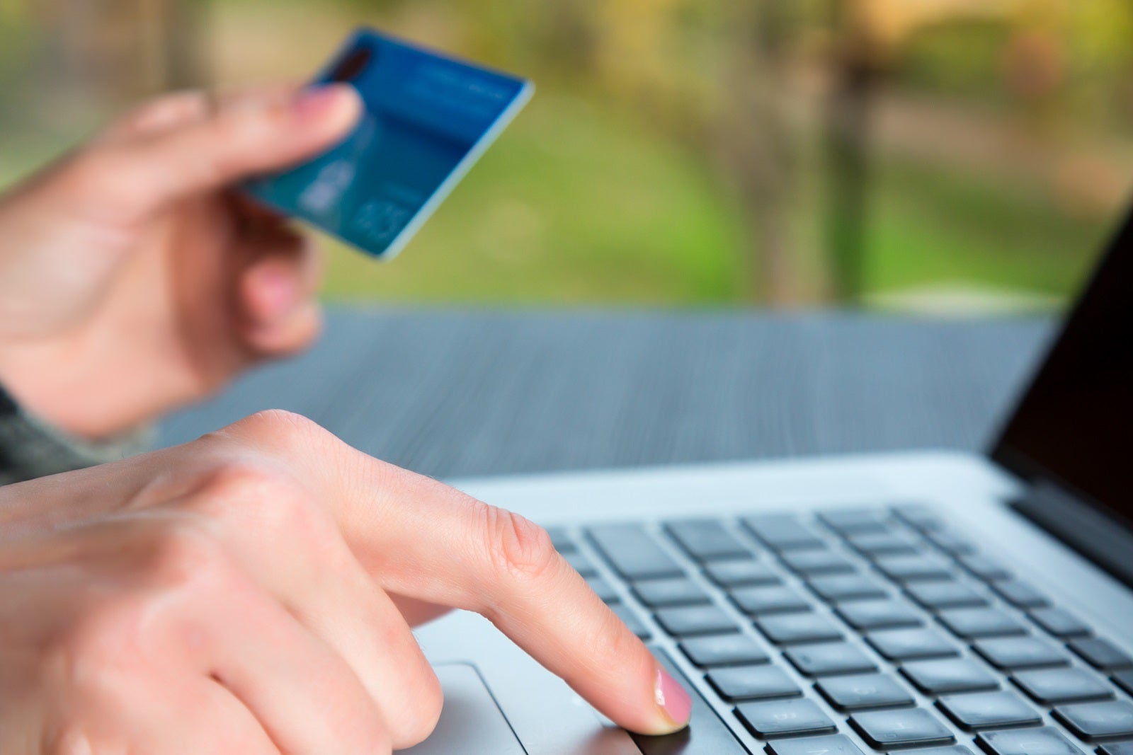 A person's hands, one holding a gift card or credit card and one buying something on a silver laptop