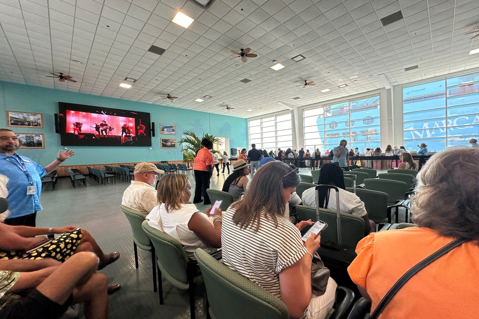 A large room with people sitting in chairs waiting to board a cruise ship