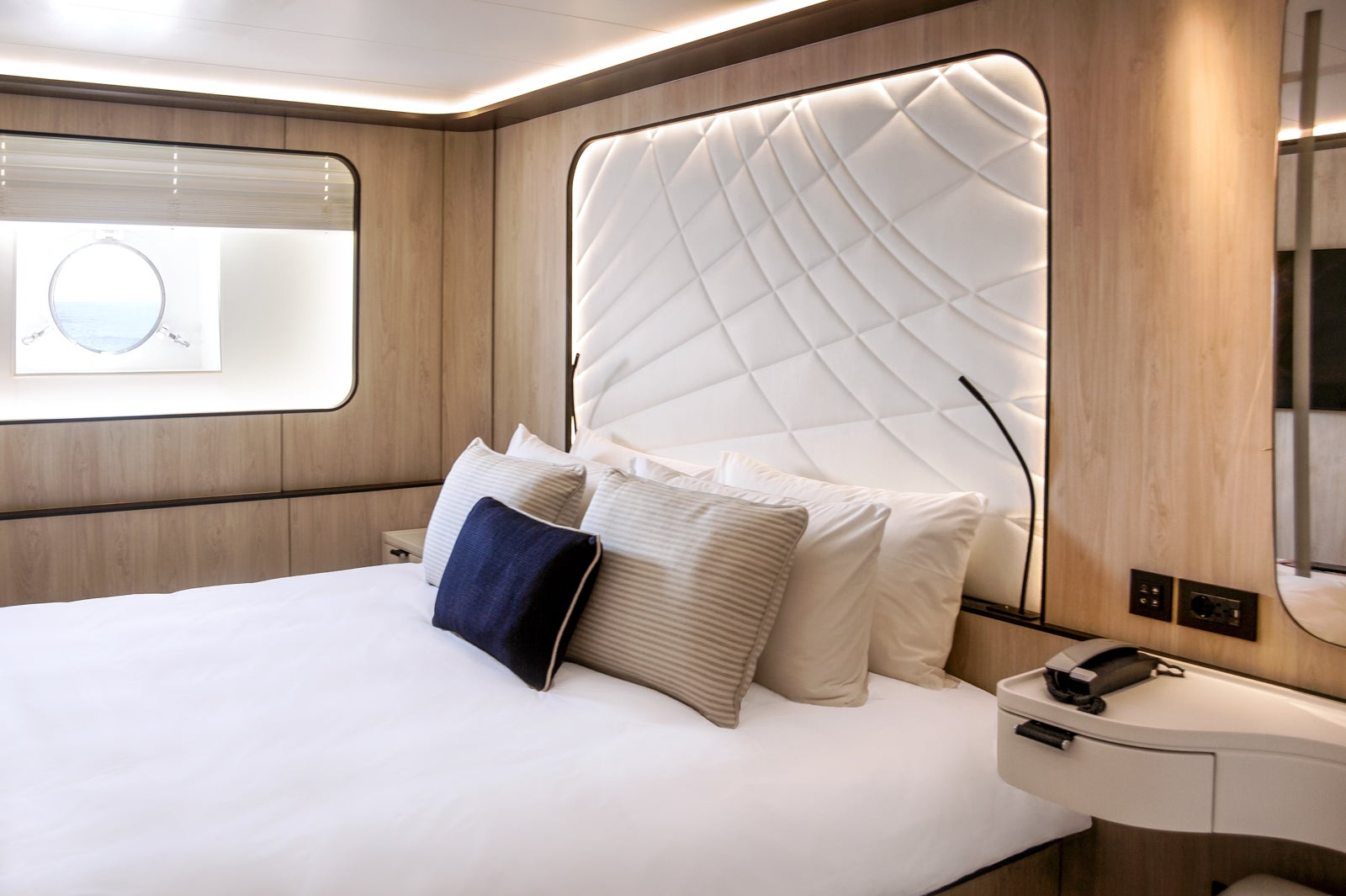 A modern cabin with white padded headboard and light wood walls.