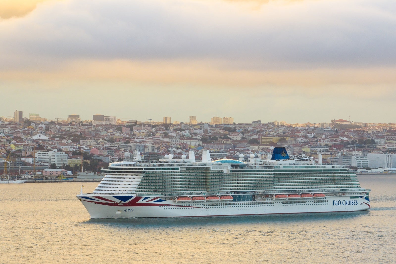 A cruise ship sailing along a coastline with a Union Flag on its hull