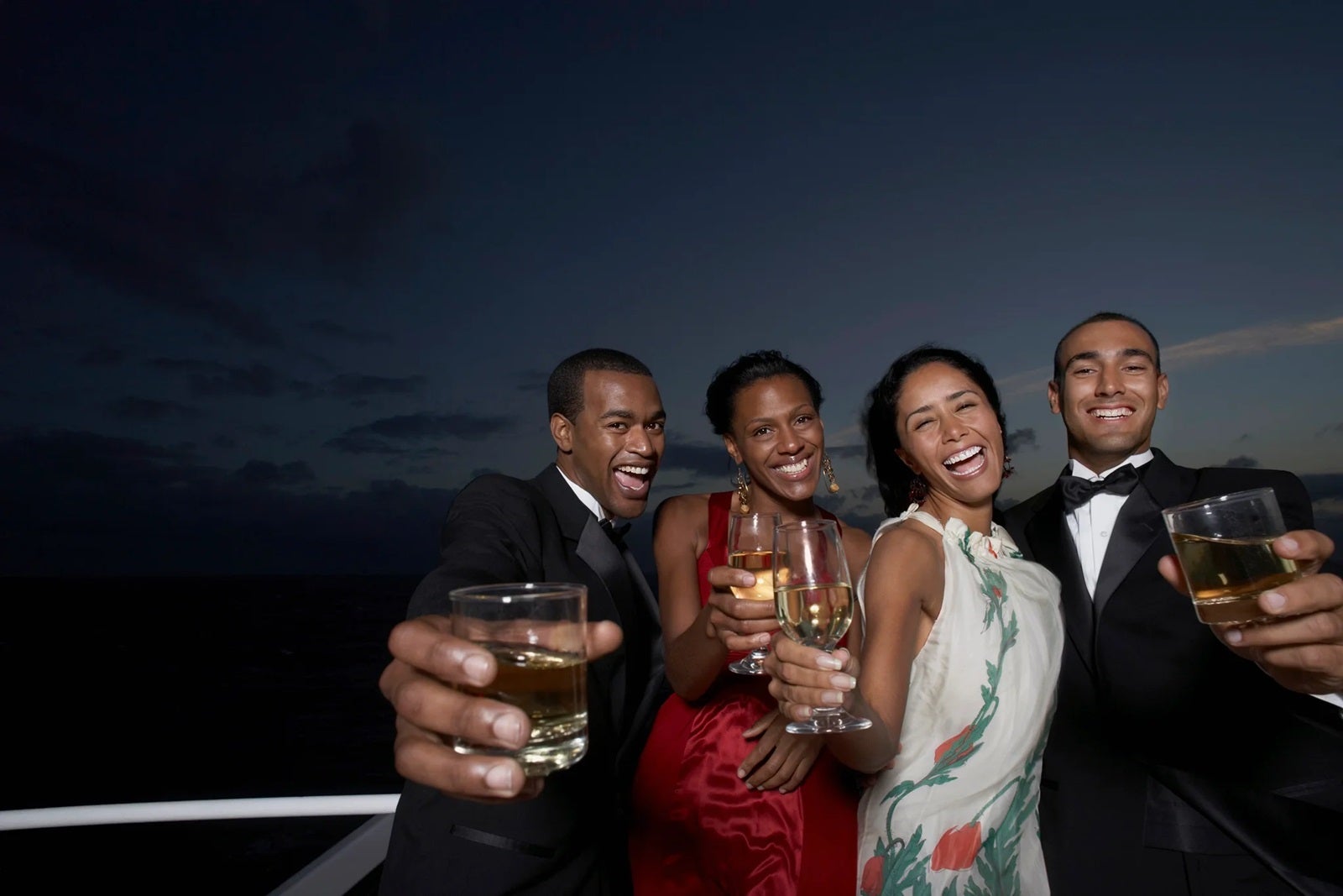 A group of young people standing on a cruise ship in formalwear holding drinks in a toast toward the camera