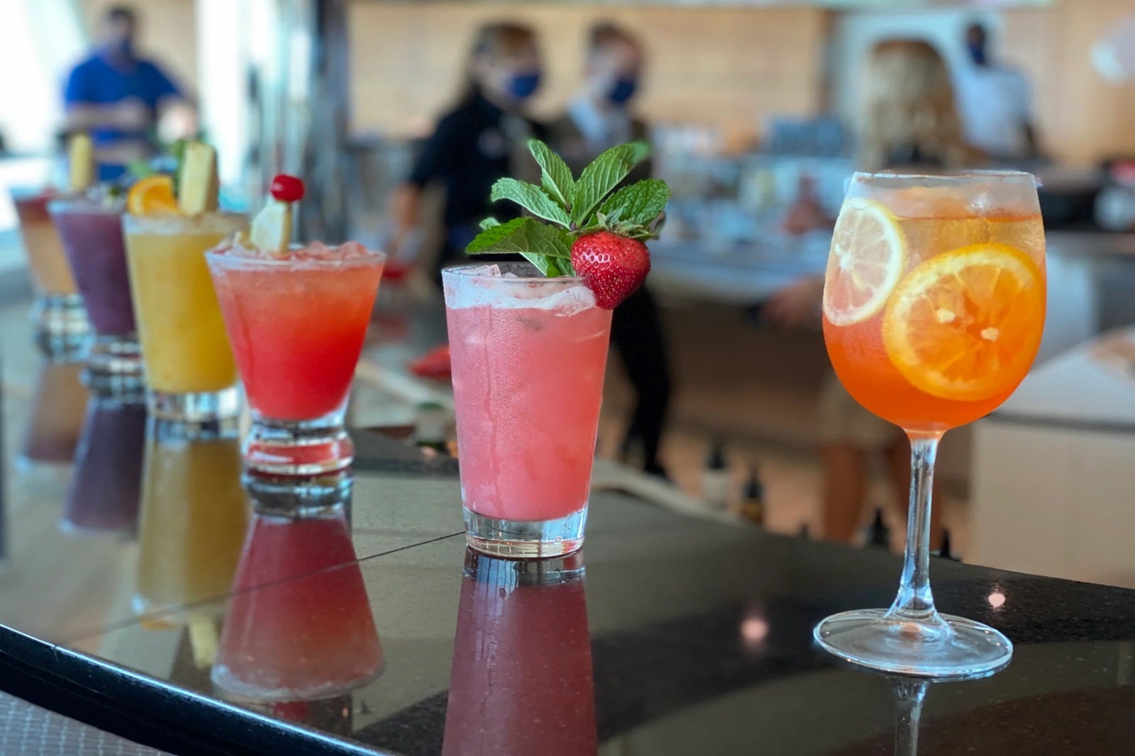 Six colorful cocktails with garnishes lined up along the top of a bar