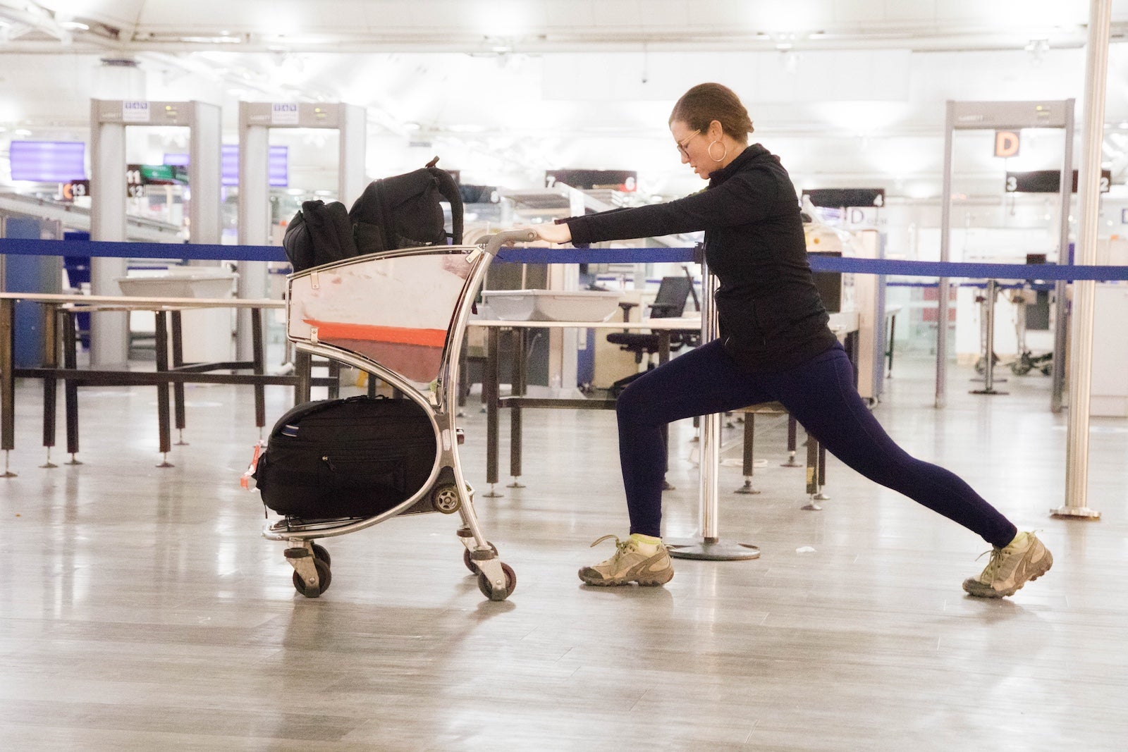 Young woman stretching at airport using her baggage cart