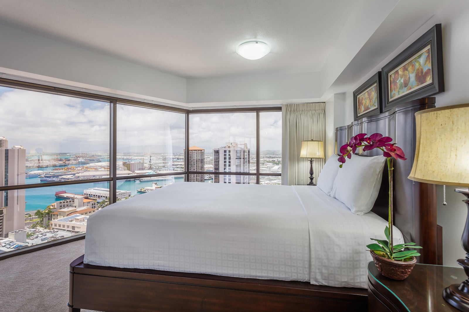 Hawaii hotel room with bed with white linens and walls of windows overlooking the water